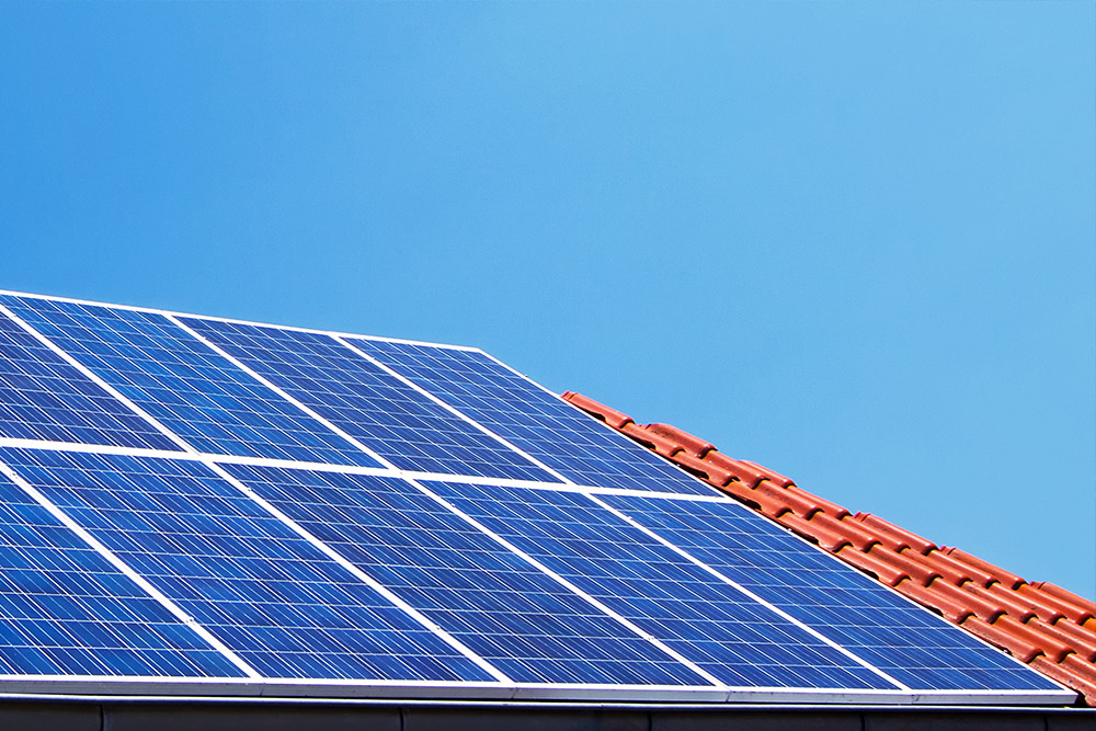 Auf einem roten, von der Sonne beschienenen Dach befinden sich mehrere Solarpaneele. Diese stehen für die Solar Dachanlagen aus Meisterhand von Meister Solar.